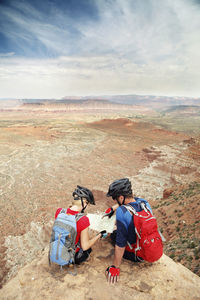 Couple reading map while sitting on cliff against sky