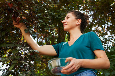 Side view of young woman picking fruits from tree