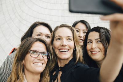 Smiling businesswoman taking selfie with female professionals at office during conference event