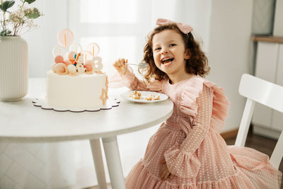 A laughing little girl eats a birthday cake on her birthday at home