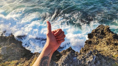 Cropped tattooed hand of man gesturing peace sign against sea