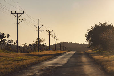 Road amidst trees on field against sky during sunset