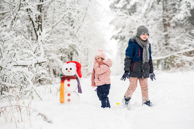 Siblings standing with snowman on snowy land