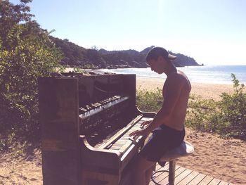 Man playing piano by beach on sunny day