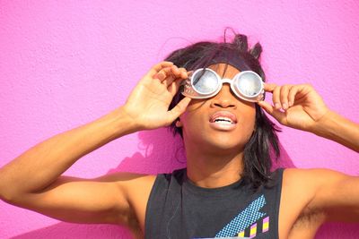 Portrait of young woman holding sunglasses against pink wall