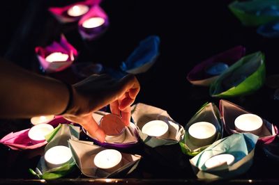 Cropped hand burning tea lights in paper boats at night