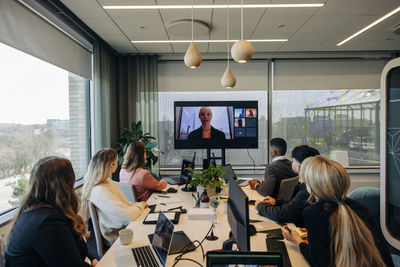 Businesswoman conducting video call with male and female colleagues sitting at desk in coworking office