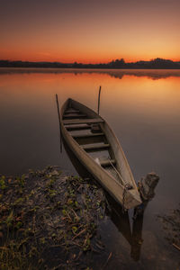 Boat moored at shore against sky during sunset