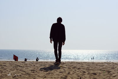 Rear view of man walking at beach against clear sky