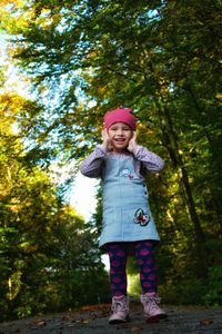 Full length of a smiling girl standing against trees