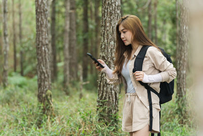 Young woman using mobile phone while standing in forest