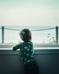 Rear view of boy looking through window