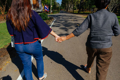 Rear view of father and daughter holding hands while walking on road