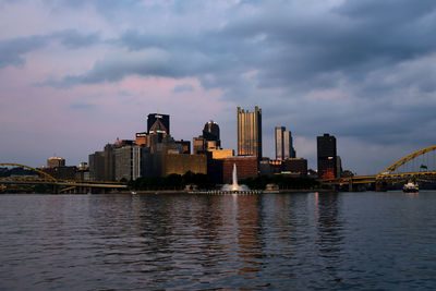 View of city at waterfront against cloudy sky