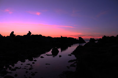 Silhouette rocks on shore against sky during sunset