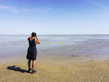 Rear view of woman standing at beach against sky