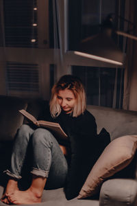 Woman reading book while sitting on sofa at home