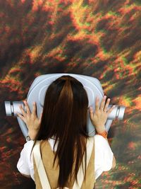 Rear view of woman looking through coin-operated binoculars at sky