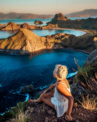 Rear view of woman sitting on rock by sea