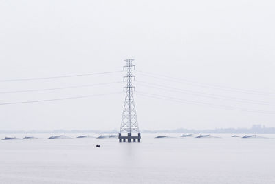 Electricity pylon in sea against sky during winter