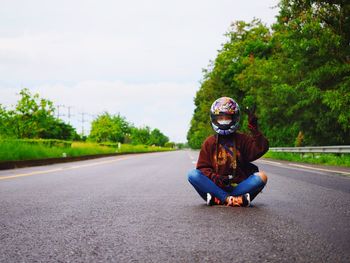 Man riding motorcycle sitting on road against sky