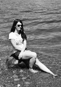 Full length of young woman sitting on rock in river
