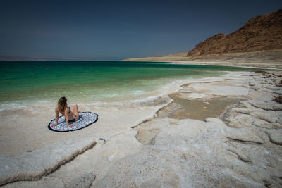 Man sitting on shore at beach against sky