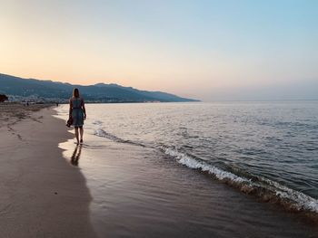 Rear view of man walking on beach during sunset