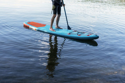 Man faceless in thermo suit paddling stand up paddleboard blue sup on water lake with paddle legs 