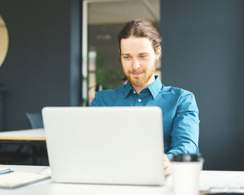 Happy young male office employee working on laptop computer