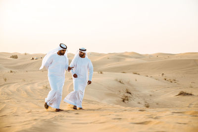 Man walking on sand dune in desert against sky