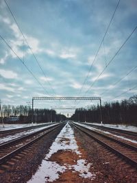 Snow covered railroad tracks against cloudy sky at dusk