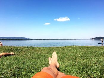 Low section of woman relaxing at beach against sky