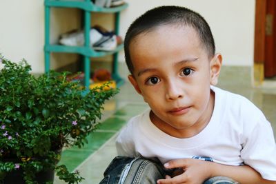 Close-up portrait of boy sitting by potted plant