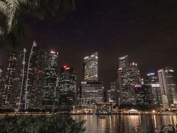 Illuminated buildings by river against sky at night