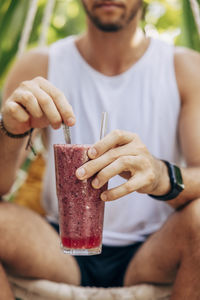 Midsection of man stirring berry smoothie while sitting at wellness resort