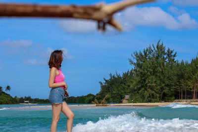Side view of woman standing on shore against blue sky