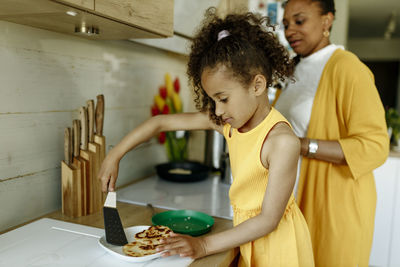 Girl helping mother cooking at kitchen counter