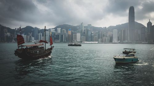 Nautical vessel on sea by cityscape against sky