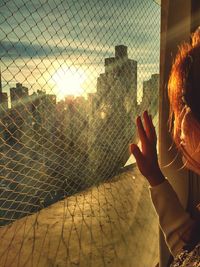 Cropped image of woman looking at sunset over buildings from window
