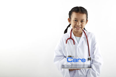 Portrait of smiling girl with stethoscope and digital tablet while standing against white background