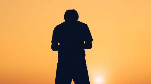 Silhouette man standing against orange sky