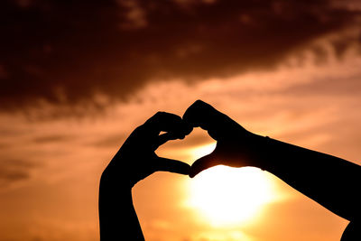 Silhouette hands making heart shape against sky during sunset