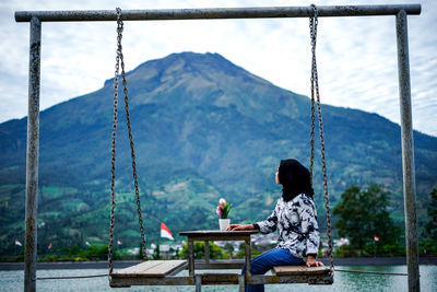 Rear view of man sitting on swing at playground