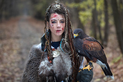 Portrait of young woman in forest with hawk perched on hand