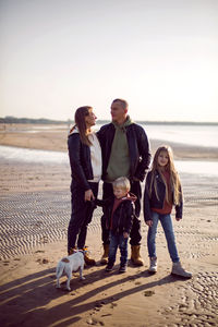 Family in a leather jacket stands along the beach with their dog in autumn