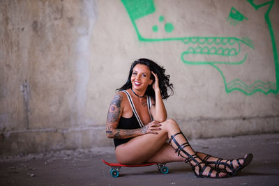 Portrait of young woman sitting against wall