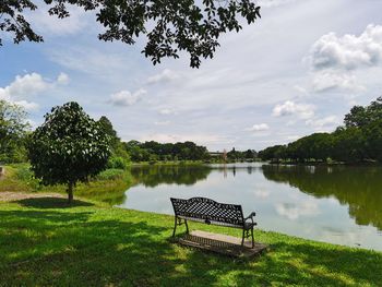 Empty bench by lake against sky