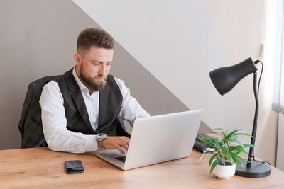 Caucasian man sits at table near laptop in office and looks at screen. serious