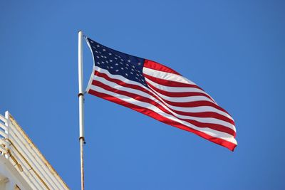 Low angle view of american flag waving against clear blue sky